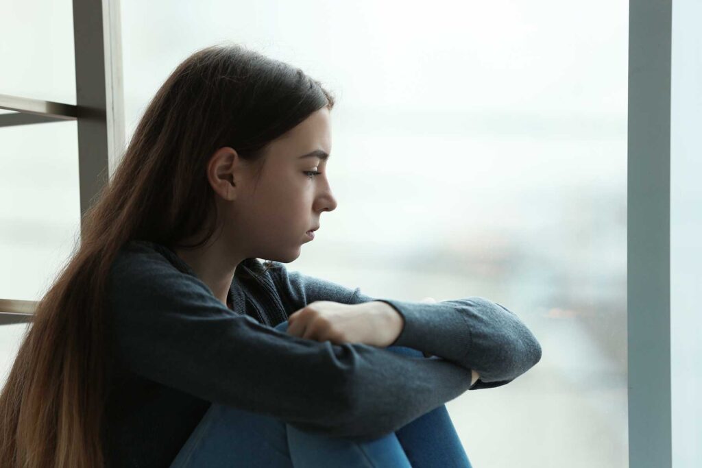 Teenager feeling depressed while looking out window in need of cognitive behavioral therapy exercises