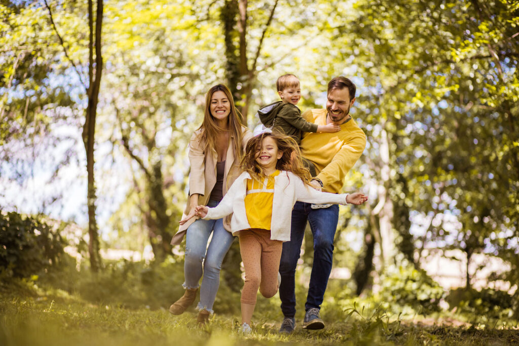 Family of four smiling while walking through a grassy wooded area and enjoying family therapy activities