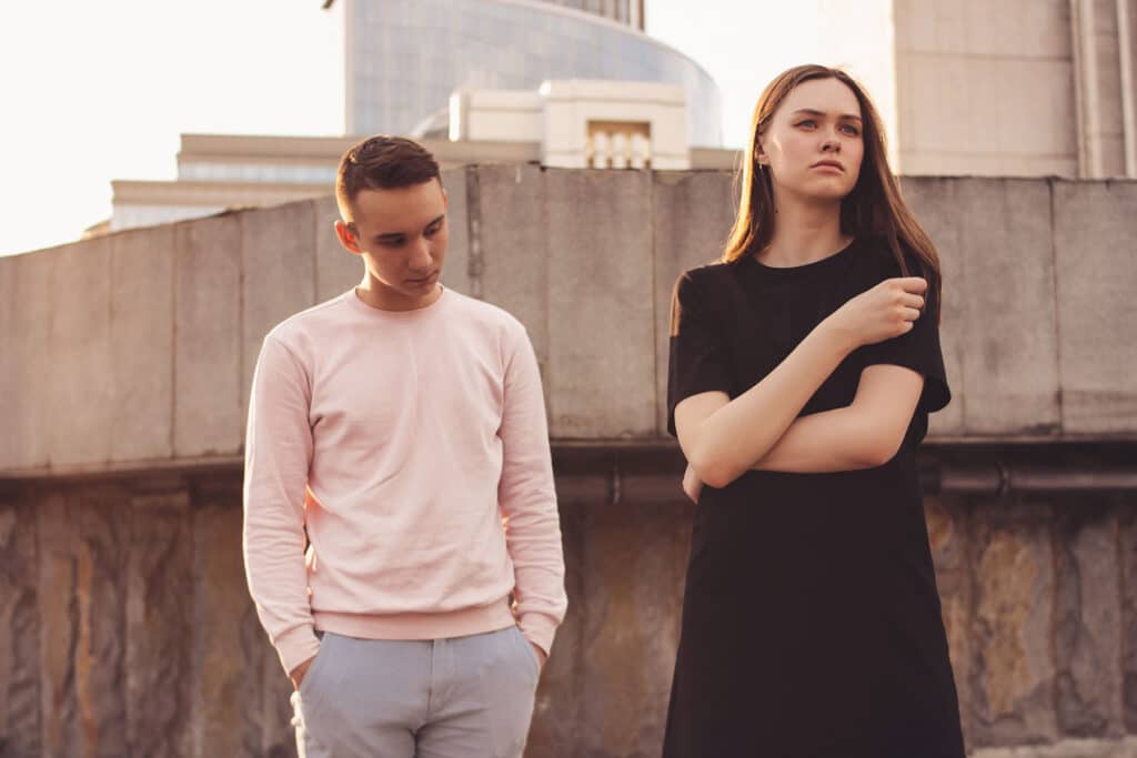 Two teenagers outside near wooden fence looking distressed while dealing with a manipulative relationship