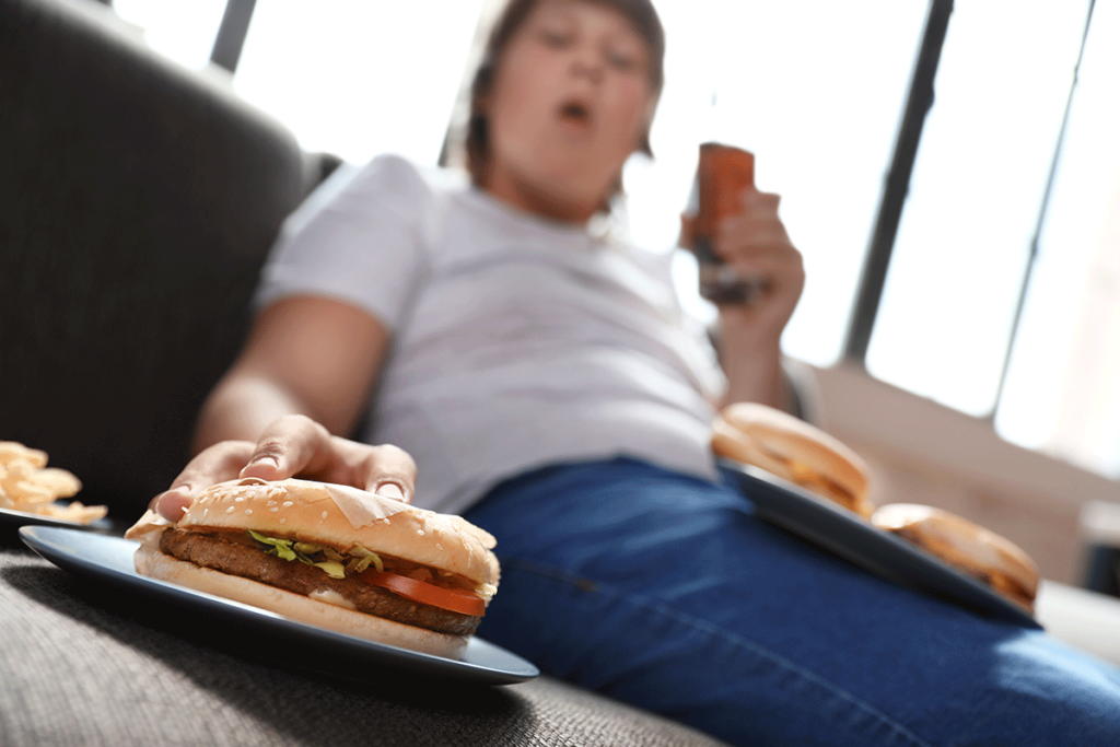 Person reaching for burger while experiencing how bipolar disorder causes binge eating