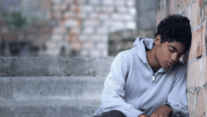 withdrawn teen sitting on steps leaning against brick wall demonstrating signs your teen needs trauma therapy