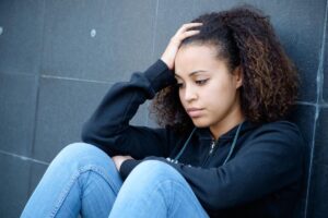 teen sitting against wall outdoors hanging head while showing signs of bipolar disorder in teenagers